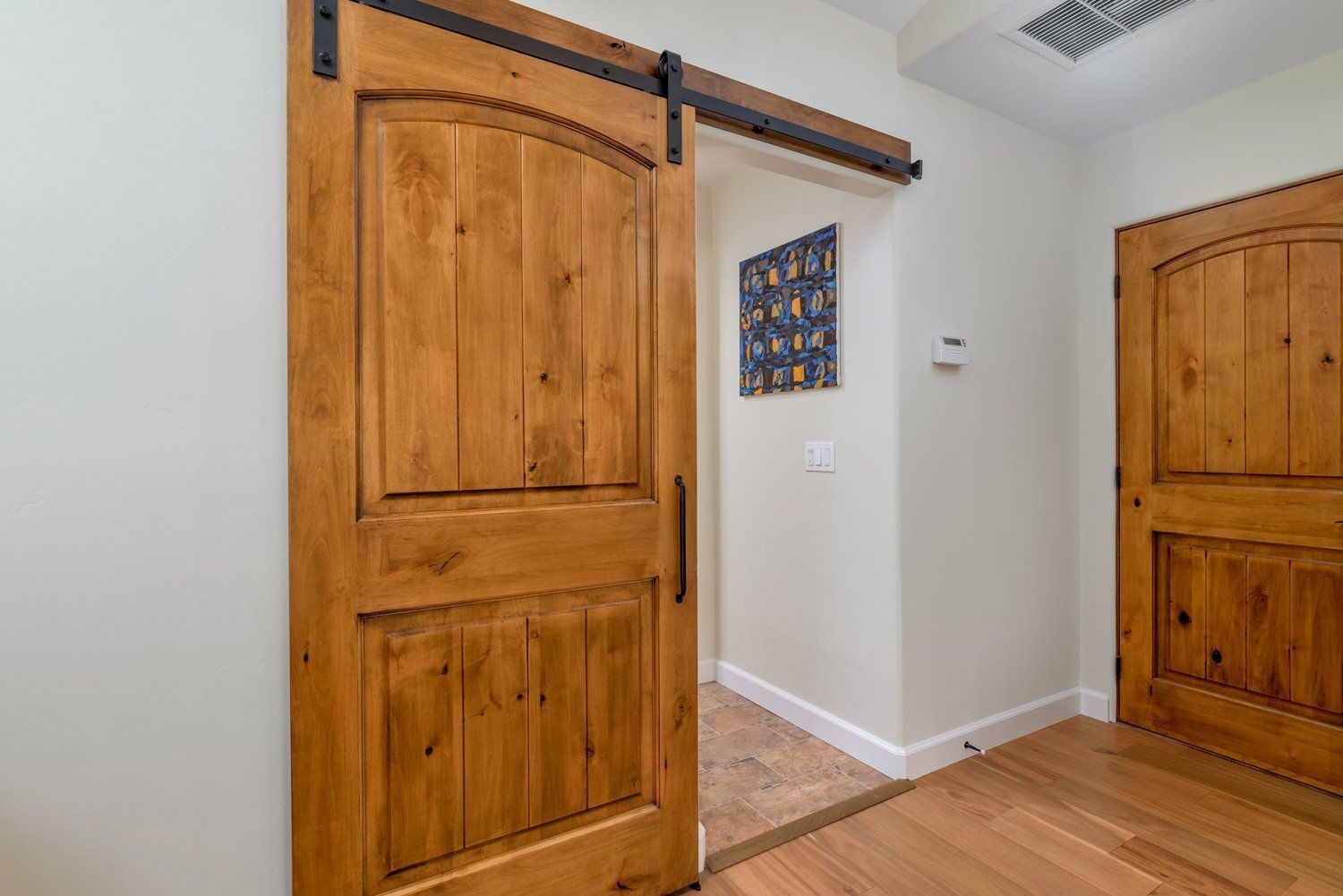 Hallway with open and closed wooden doors, hardwood floors, and white walls.