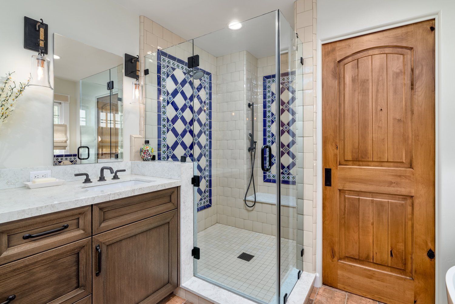 Bathroom with glass shower, blue patterned tile, wooden vanity, and wood door