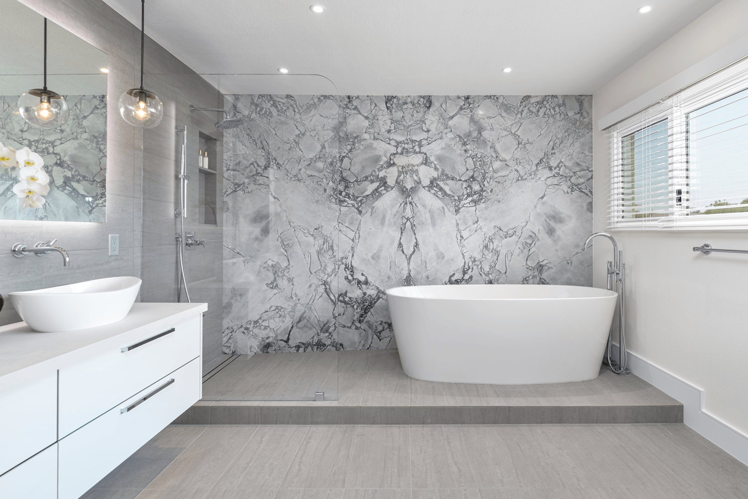 Modern gray bathroom with freestanding tub, floating vanity, and marble accent wall