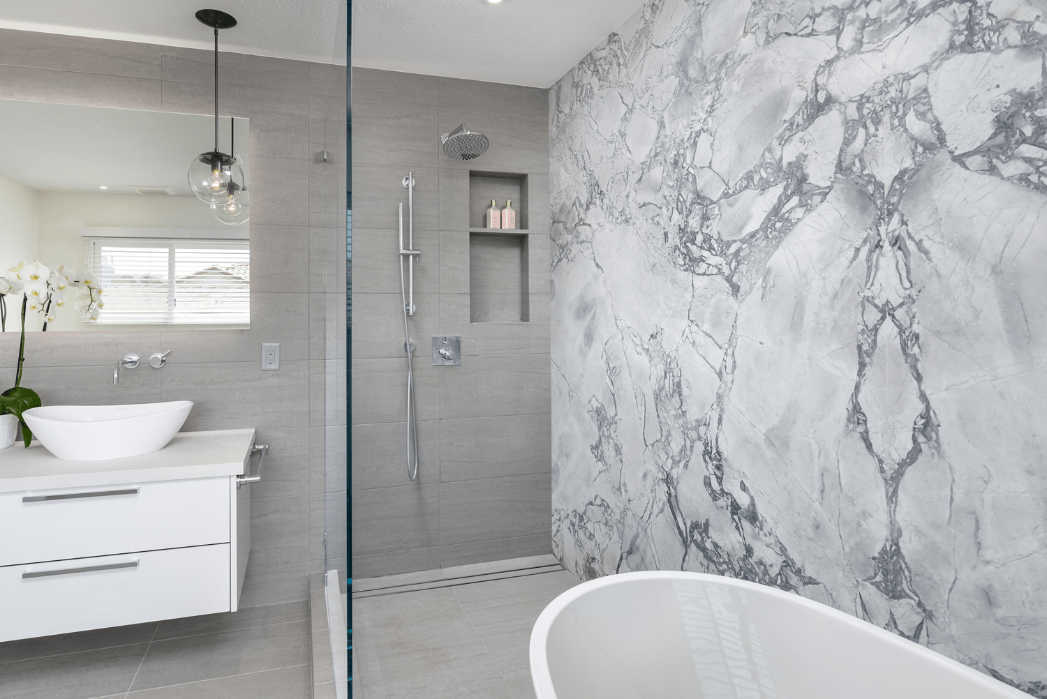 Modern bathroom with glass shower, marble-look wall, and white vanity and tub