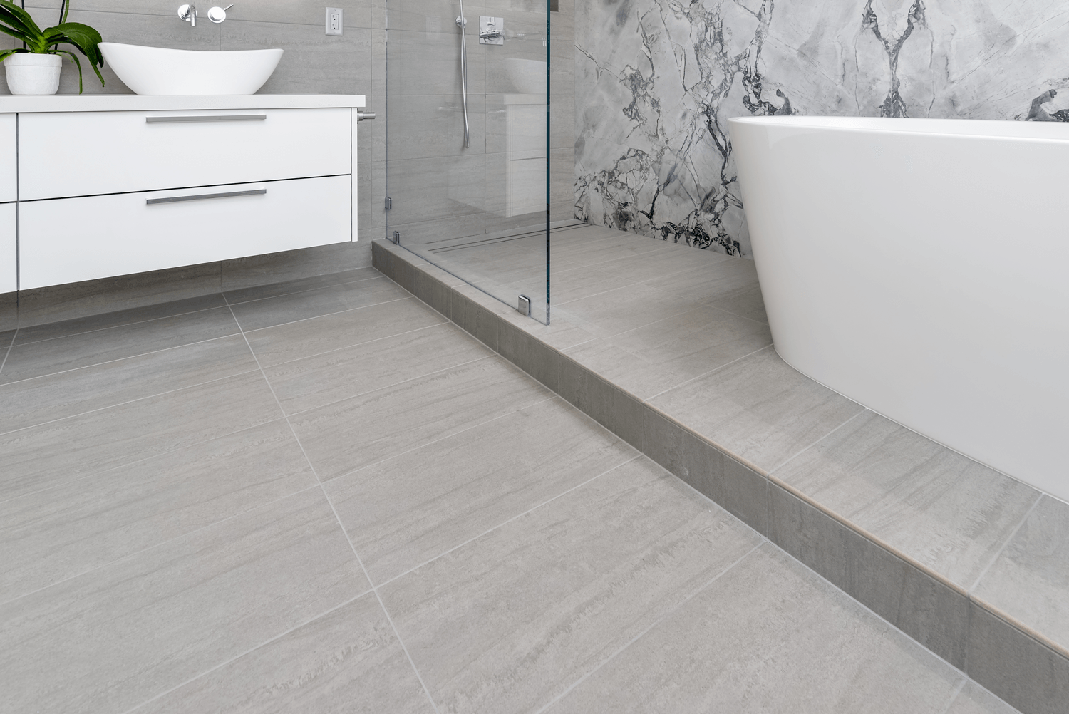 Modern bathroom with white vanity, glass shower, and freestanding tub on gray tiled floor