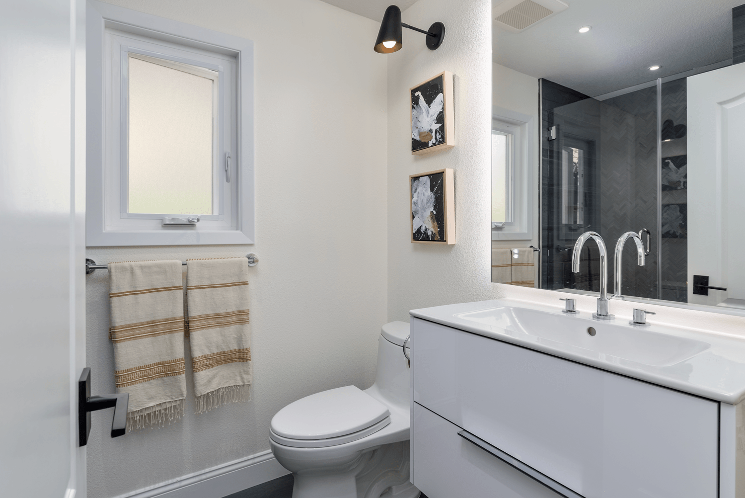 Bright modern bathroom with white vanity, mirror, toilet, towel rack, and shower