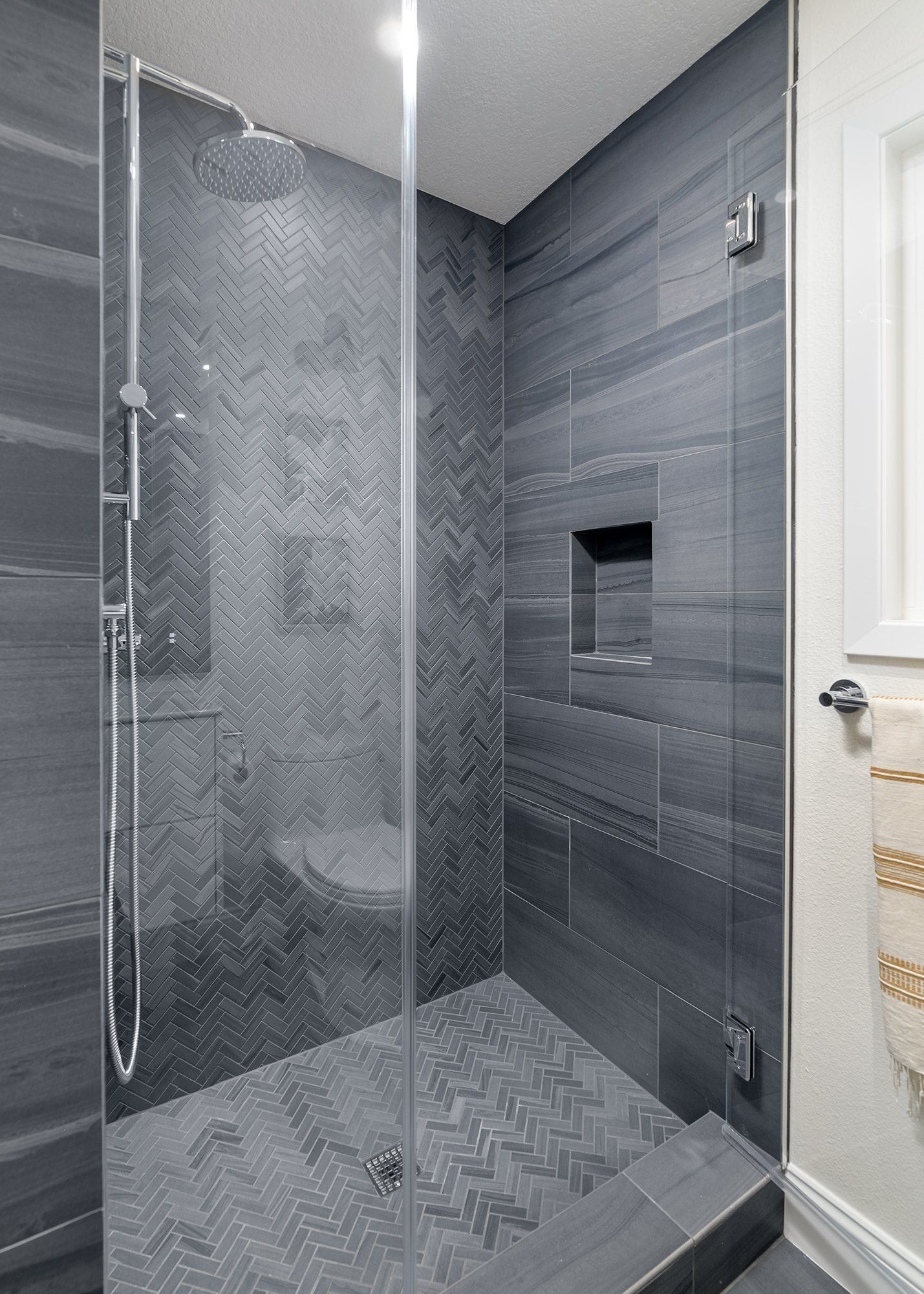 Gray tiled walk-in shower with glass door, built-in niche, and handheld showerhead.