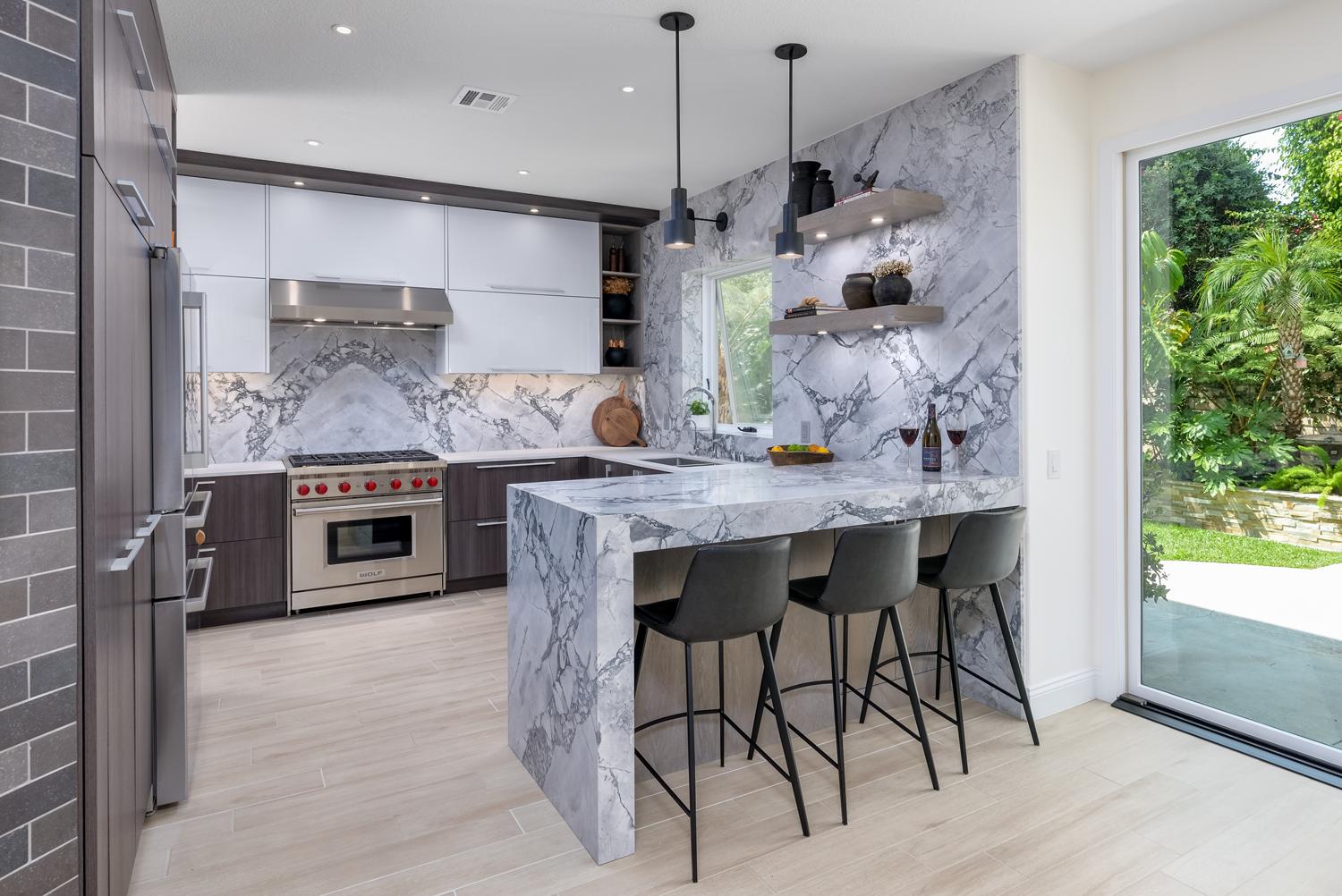 Modern white marble kitchen with island, stainless appliances, and large sliding glass door to a green garden.