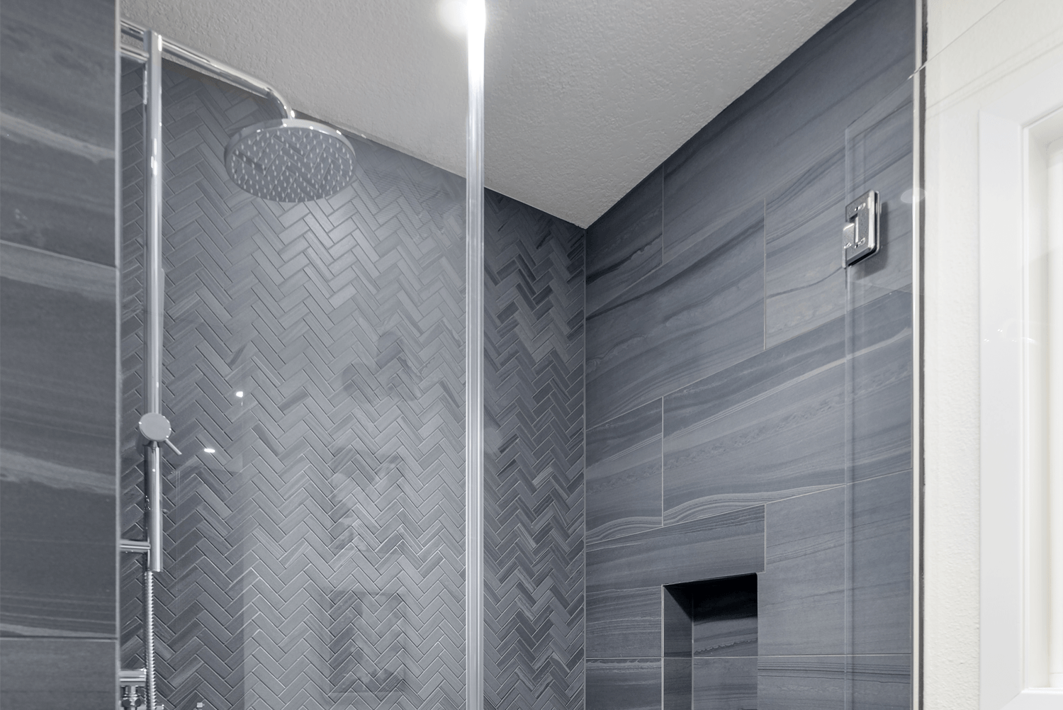 Modern gray-tiled shower with glass doors and a rainfall showerhead.