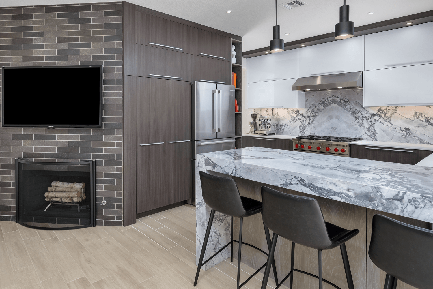 Modern kitchen and living area with marble island, bar stools, fireplace, wall-mounted TV, and stainless steel appliances