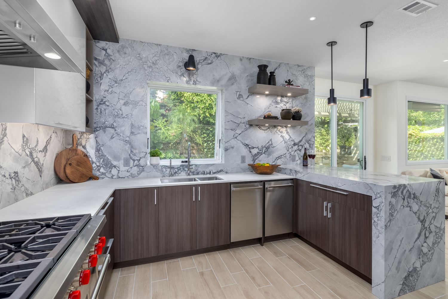 Modern kitchen with dark cabinets, marble-patterned backsplash, white counters, and large windows