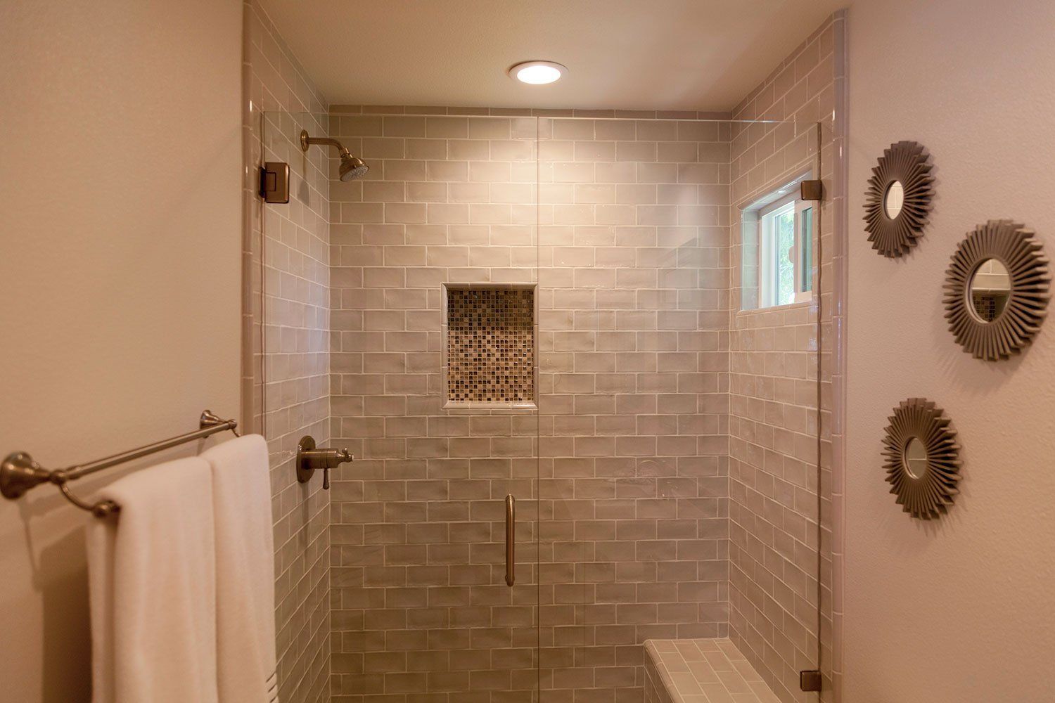 Bathroom with glass shower enclosure, beige tile walls, towel bar, and decorative wall accents