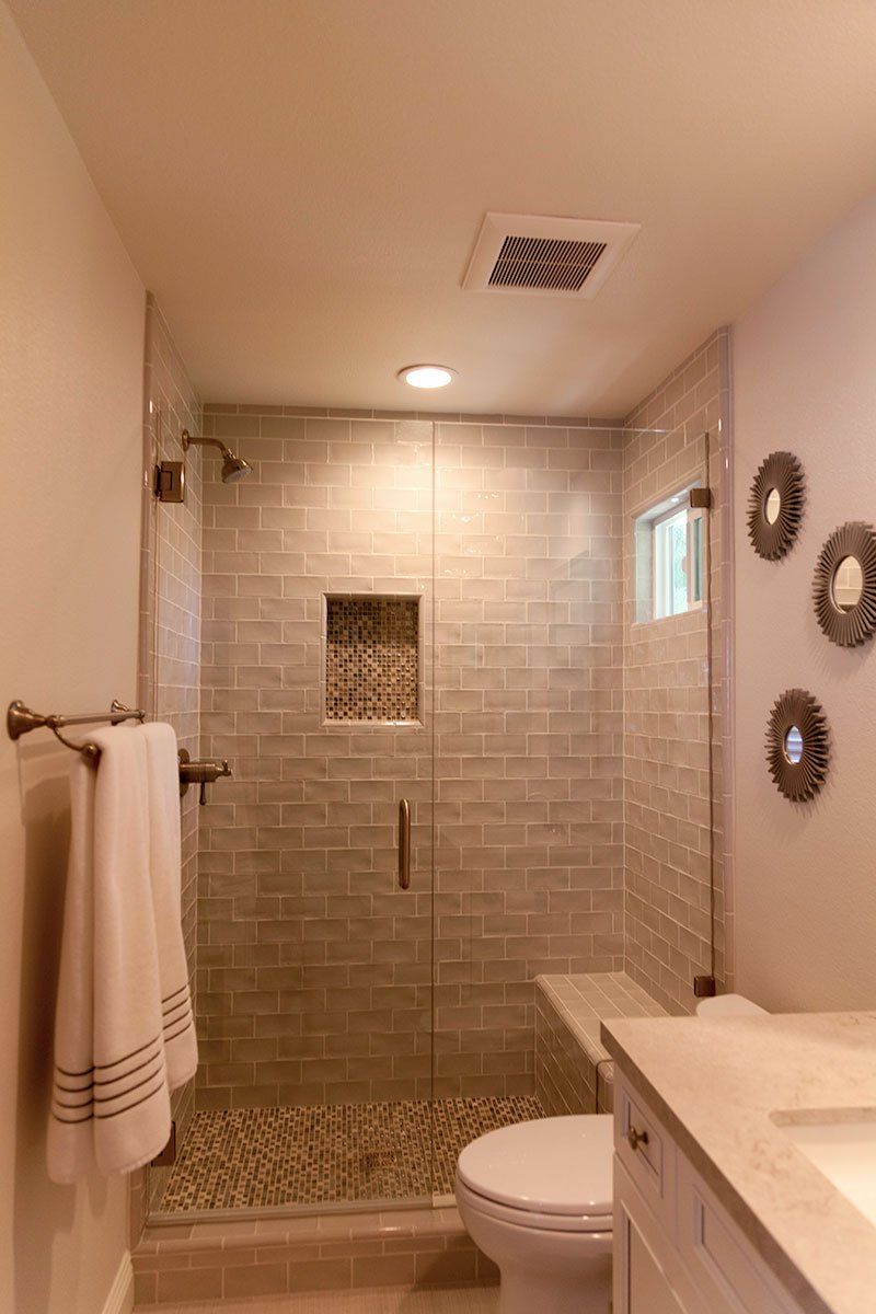 Modern bathroom with glass shower, white vanity, toilet, and beige tile walls