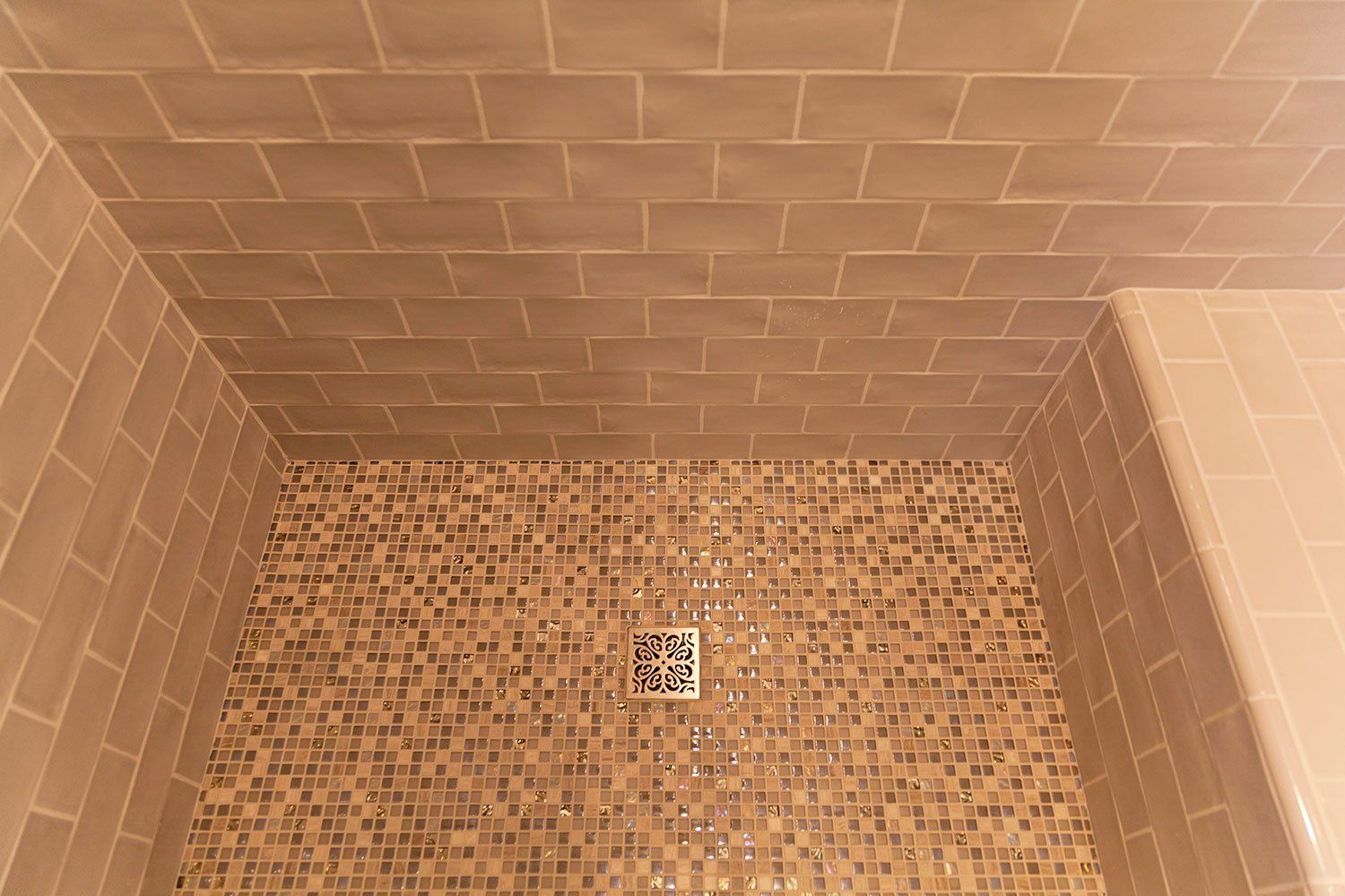 Small brown-tiled shower stall with a square drain in the center of the floor.