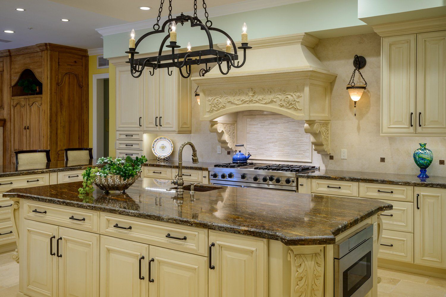 Elegant cream-colored kitchen with granite island, chandelier, and stainless steel range hood