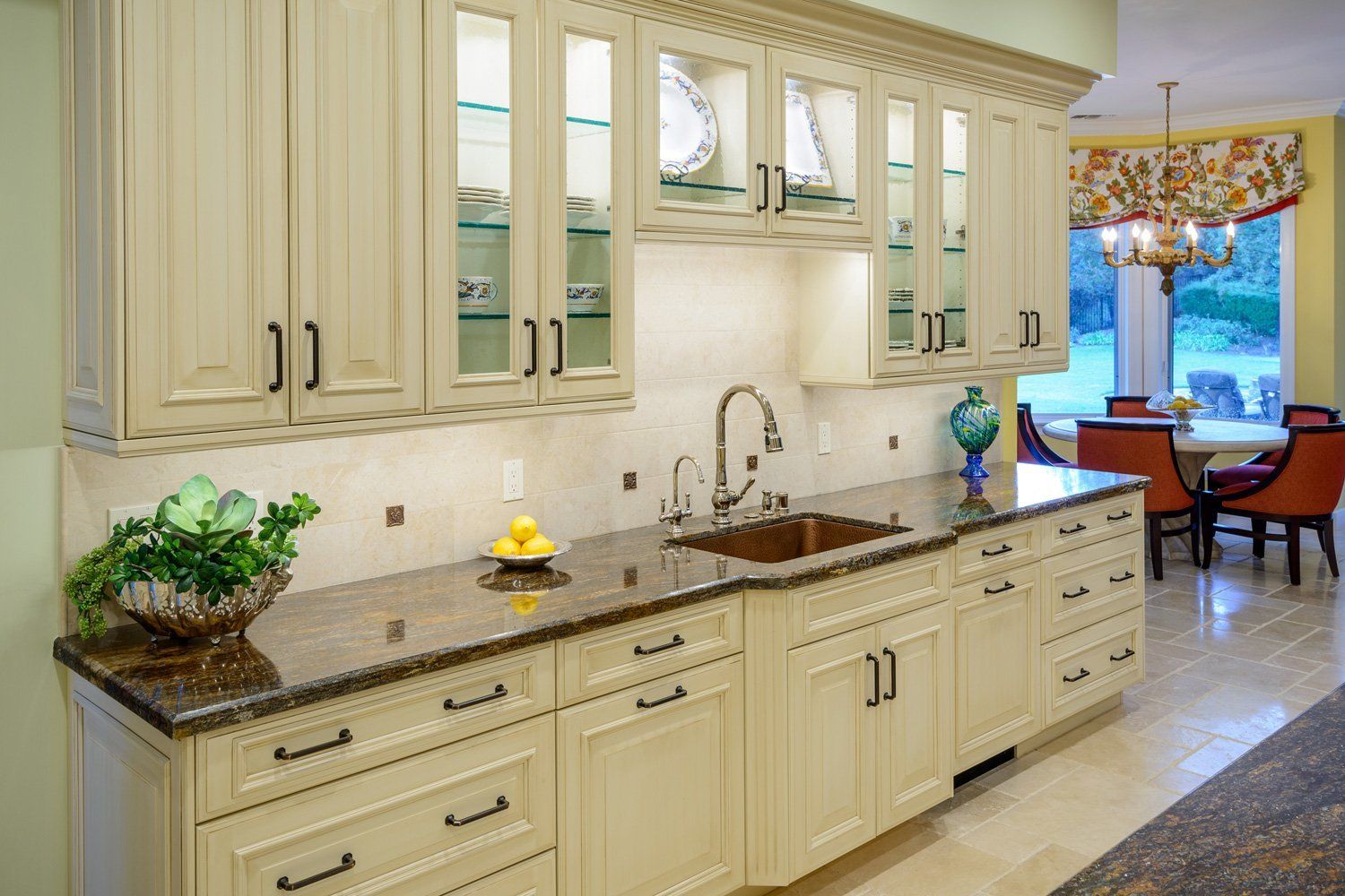 Elegant cream kitchen with marble island, dark countertops, and chandelier-lit dining area beyond