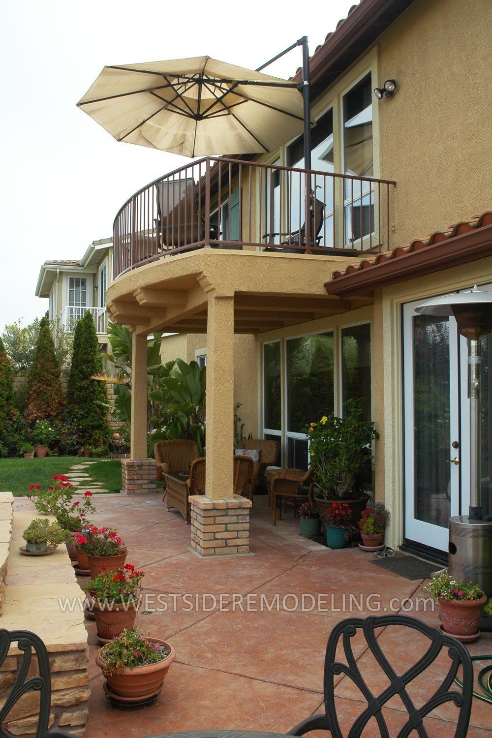 Patio with potted plants, balcony, umbrella, and sliding glass doors outside a house