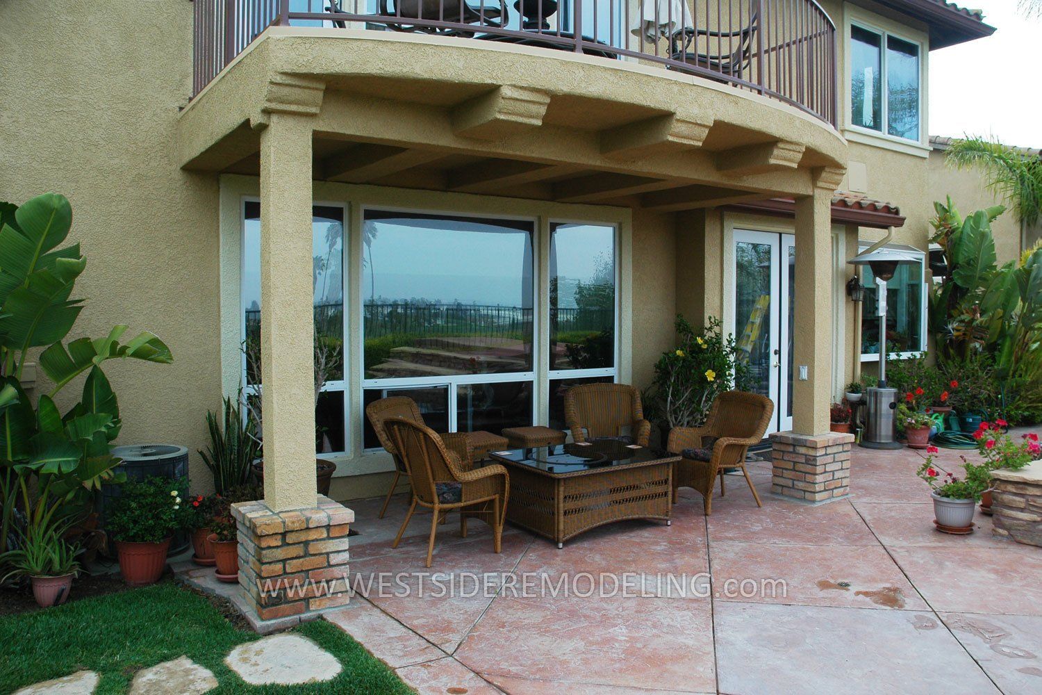 Patio with wicker chairs and potted plants outside a beige house with large glass doors
