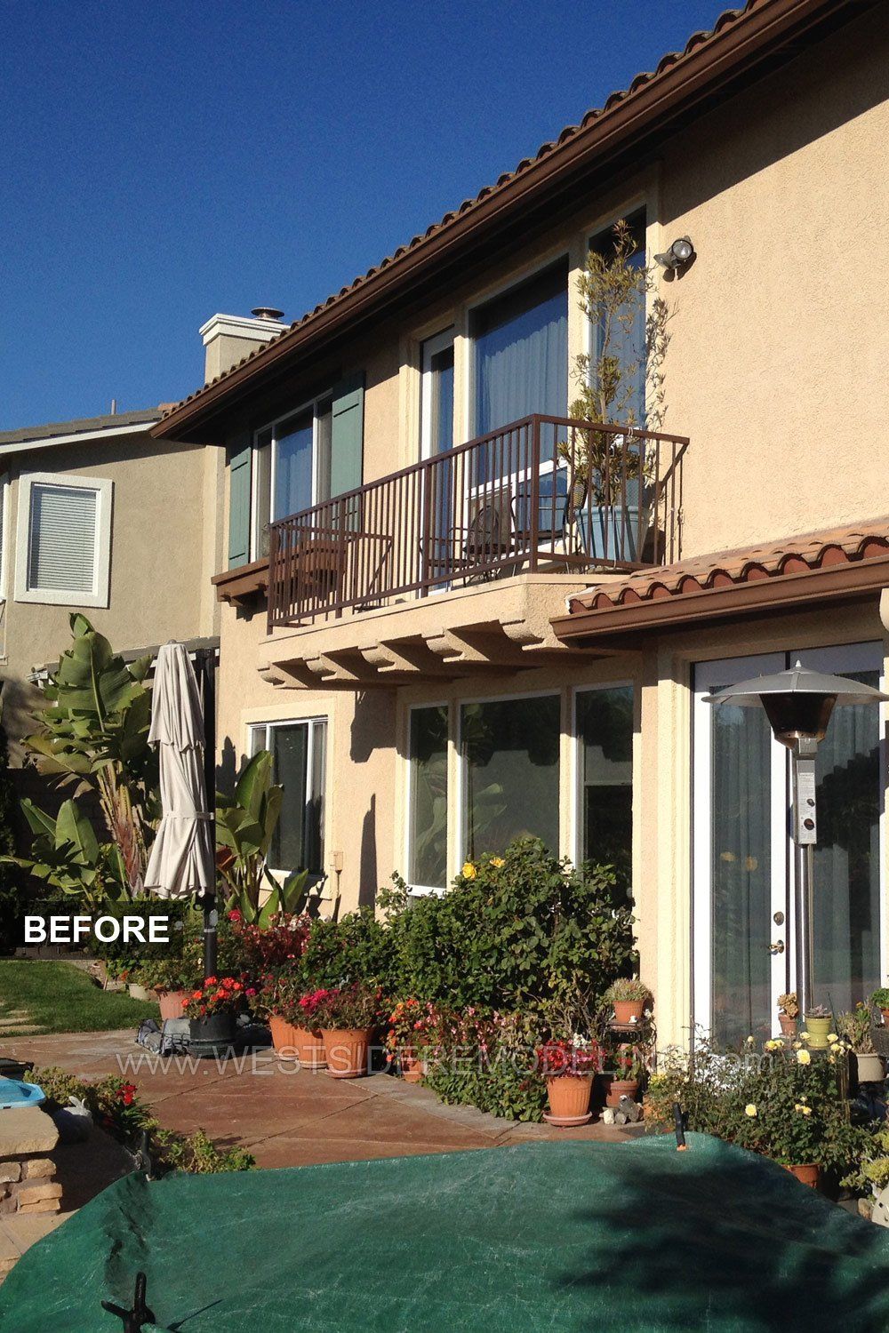 Before photo of a beige stucco house with balcony, potted plants, and a green-covered driveway