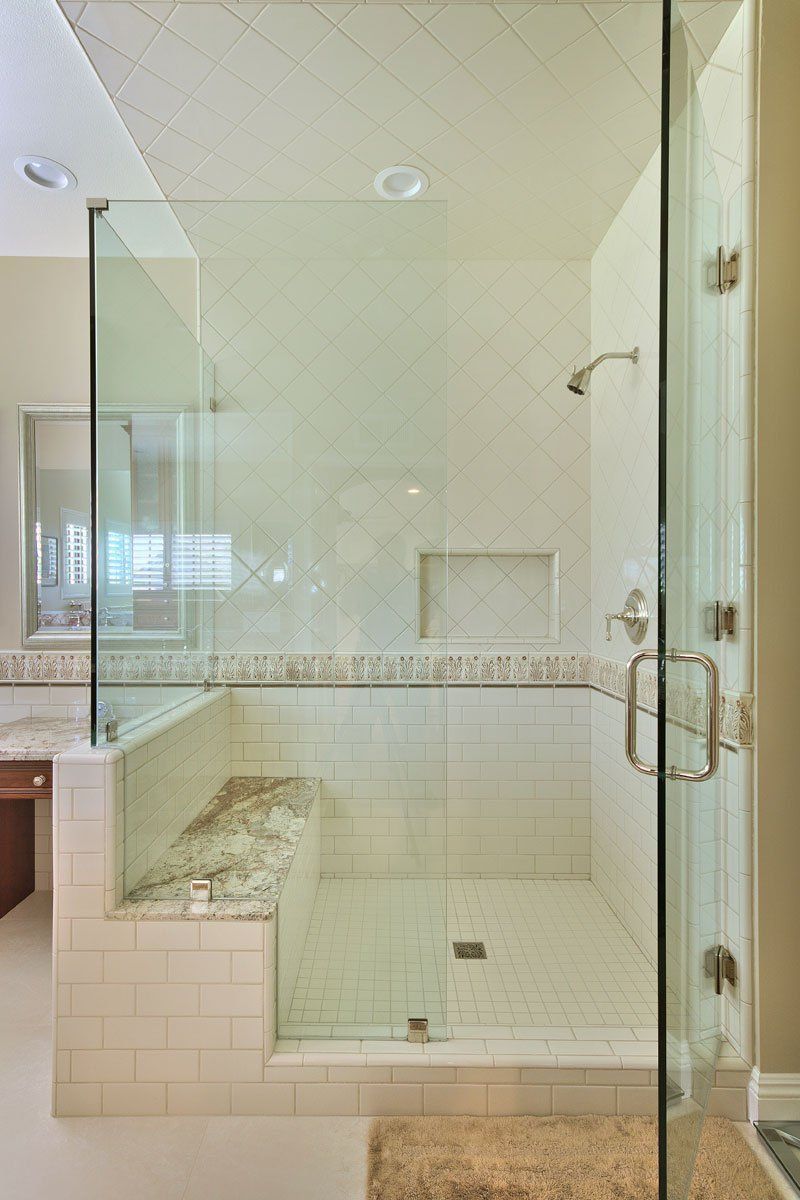 Glass walk-in shower with white tile, built-in bench, and chrome fixtures