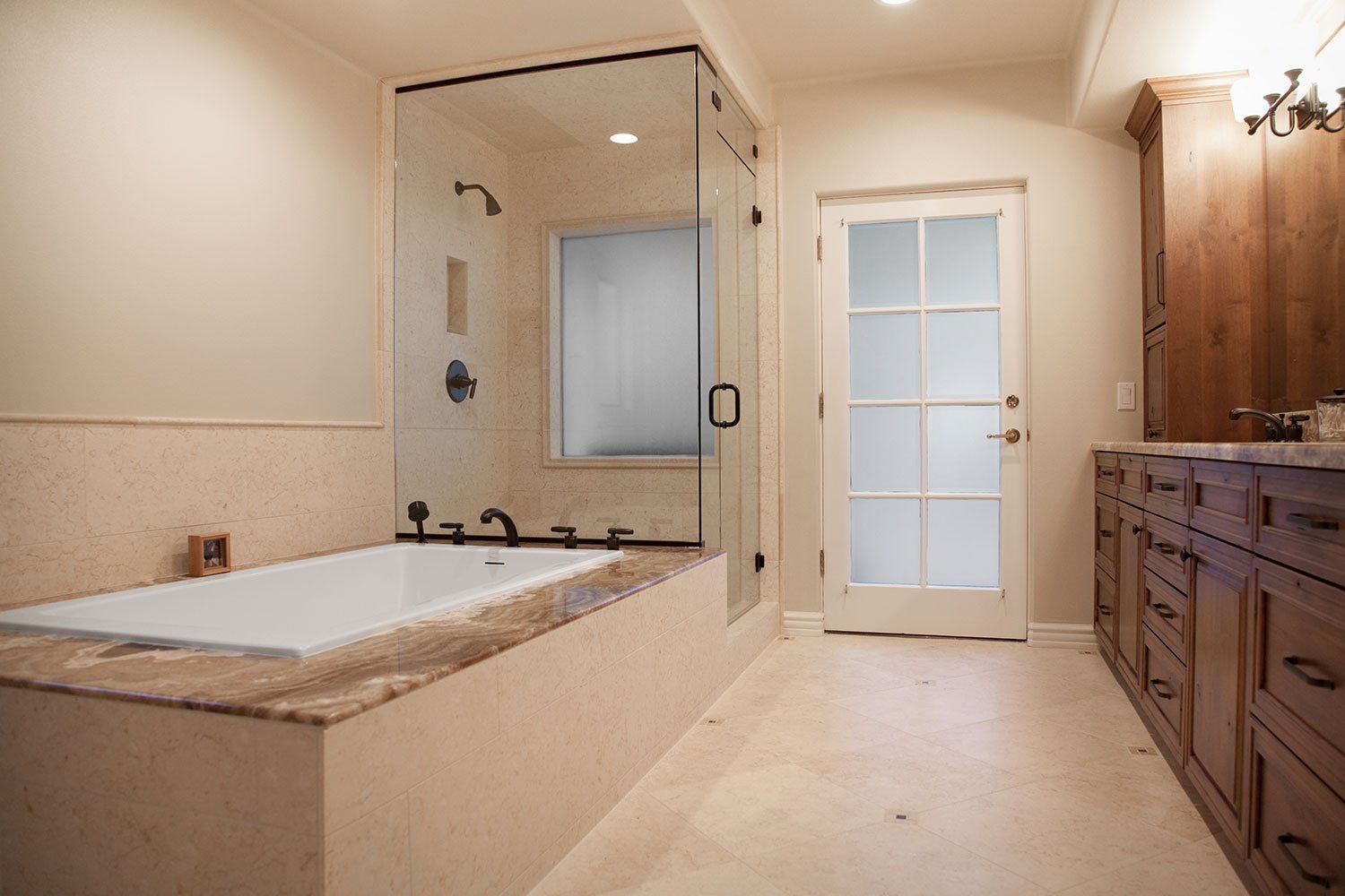 Bright bathroom with a corner soaking tub, glass shower, white tile, and wood vanity cabinets.