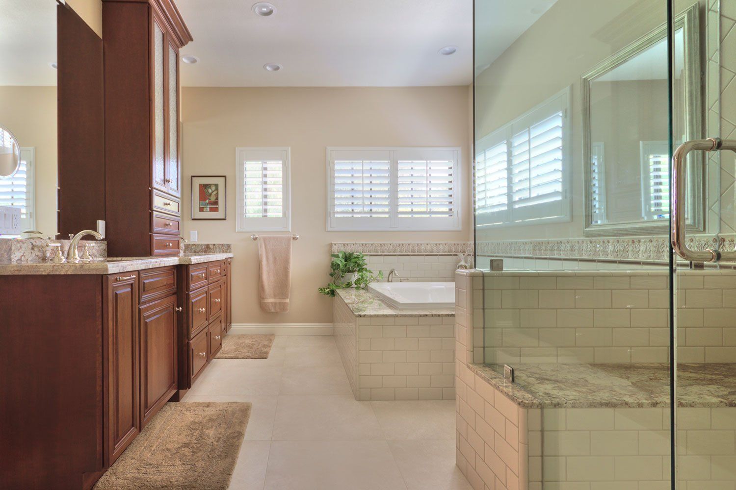 Spacious bathroom with wooden vanity, glass shower, soaking tub, and white plantation shutters