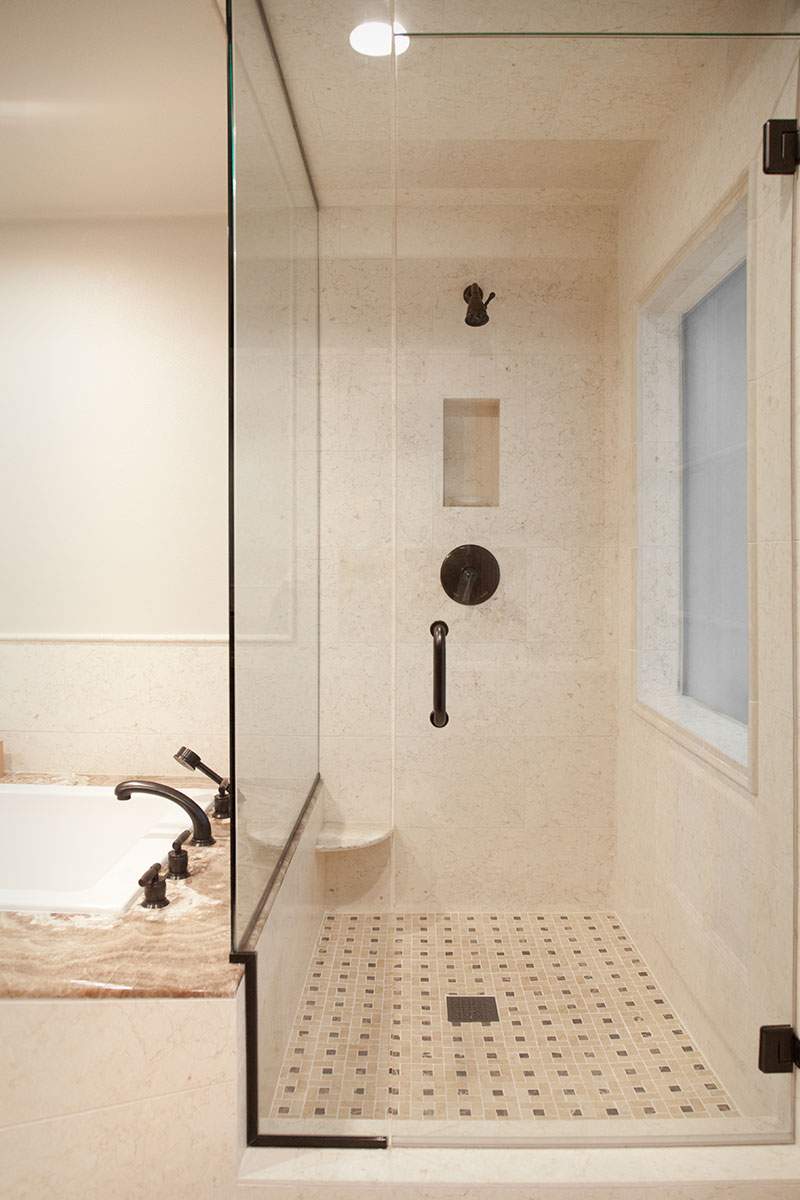 Glass-enclosed shower with white tile and black fixtures beside a vanity sink