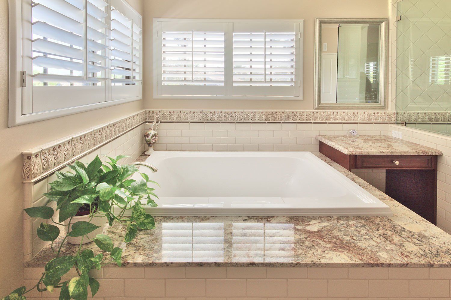 Bright bathroom with a soaking tub, granite counters, white shutters, and a potted plant