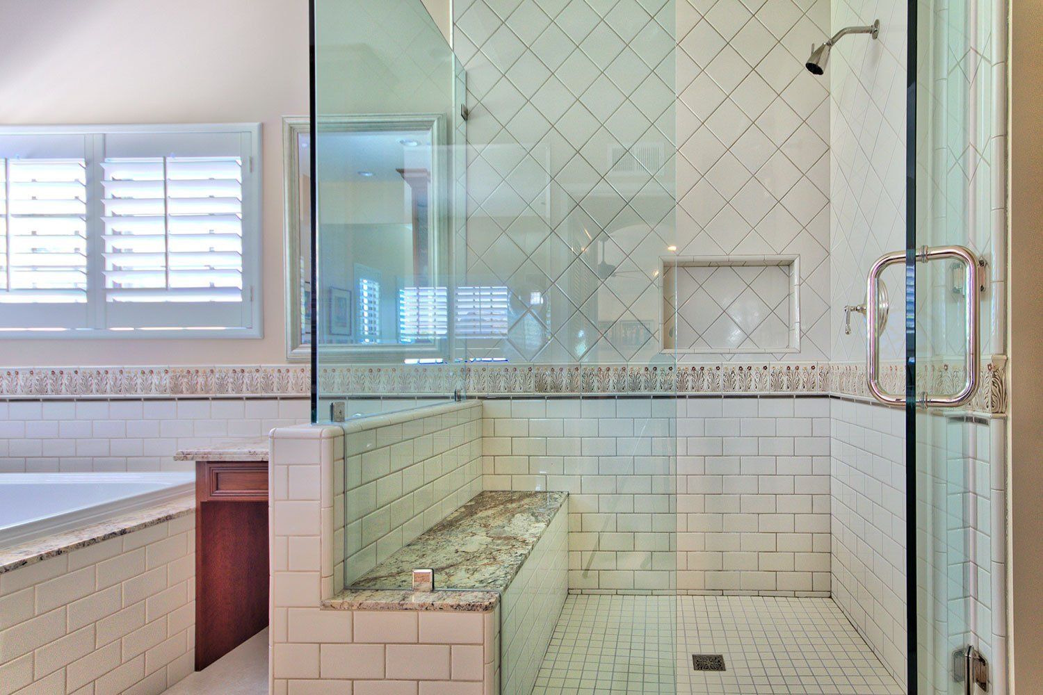 Modern bathroom with glass shower, white tile, and window above a tub