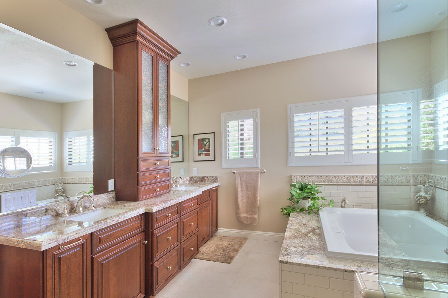 Bright bathroom with wood cabinets, granite counters, large mirror, and a freestanding tub by windows.