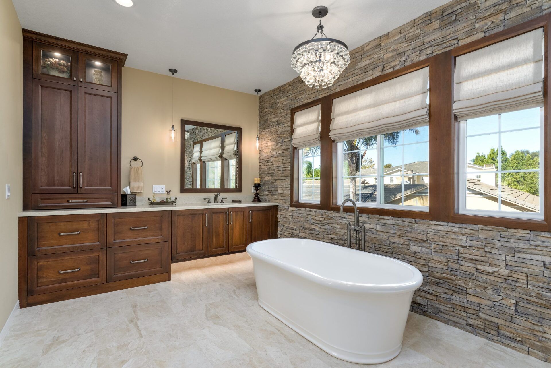 Modern bathroom with freestanding tub, dark wood cabinets, large windows, and stone accent wall
