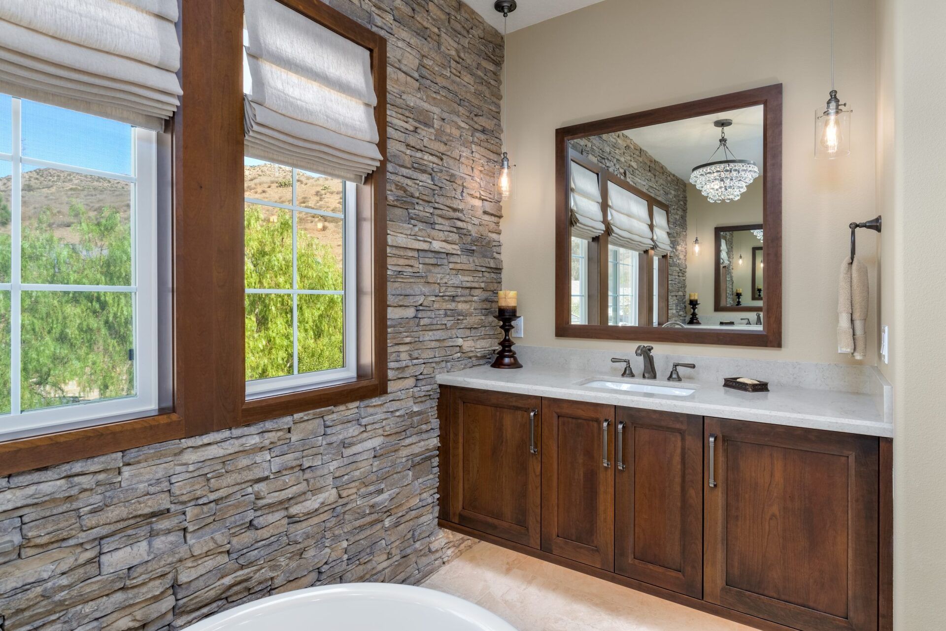 Stone-walled bathroom with double vanity, large mirror, and windows with blinds