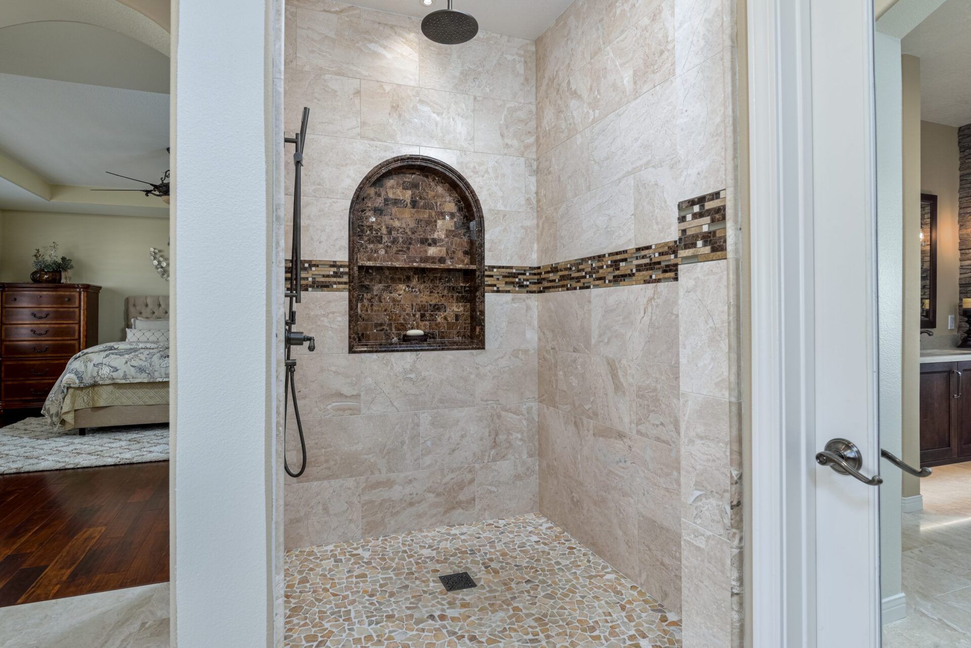 Spacious tiled walk-in shower with arched niche, pebble floor, and mosaic accent band