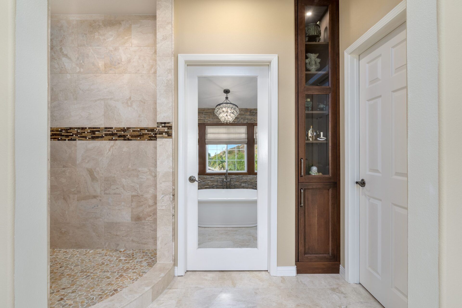 Bright tiled bathroom with a walk-in shower, white door, and dark wood cabinet.