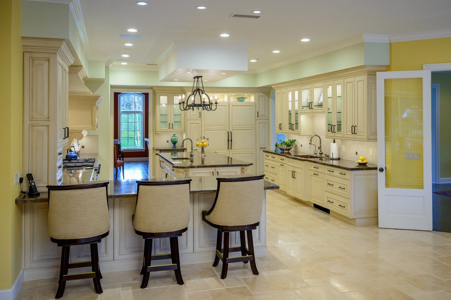 Bright cream kitchen with island, three stools, pendant lights, and glass doors to the outside.