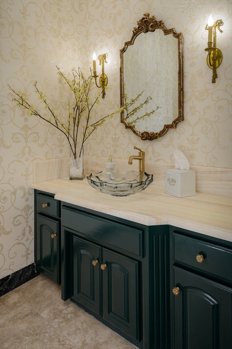 Elegant powder room vanity with dark green cabinets, marble countertop, gold sconces, and framed mirror