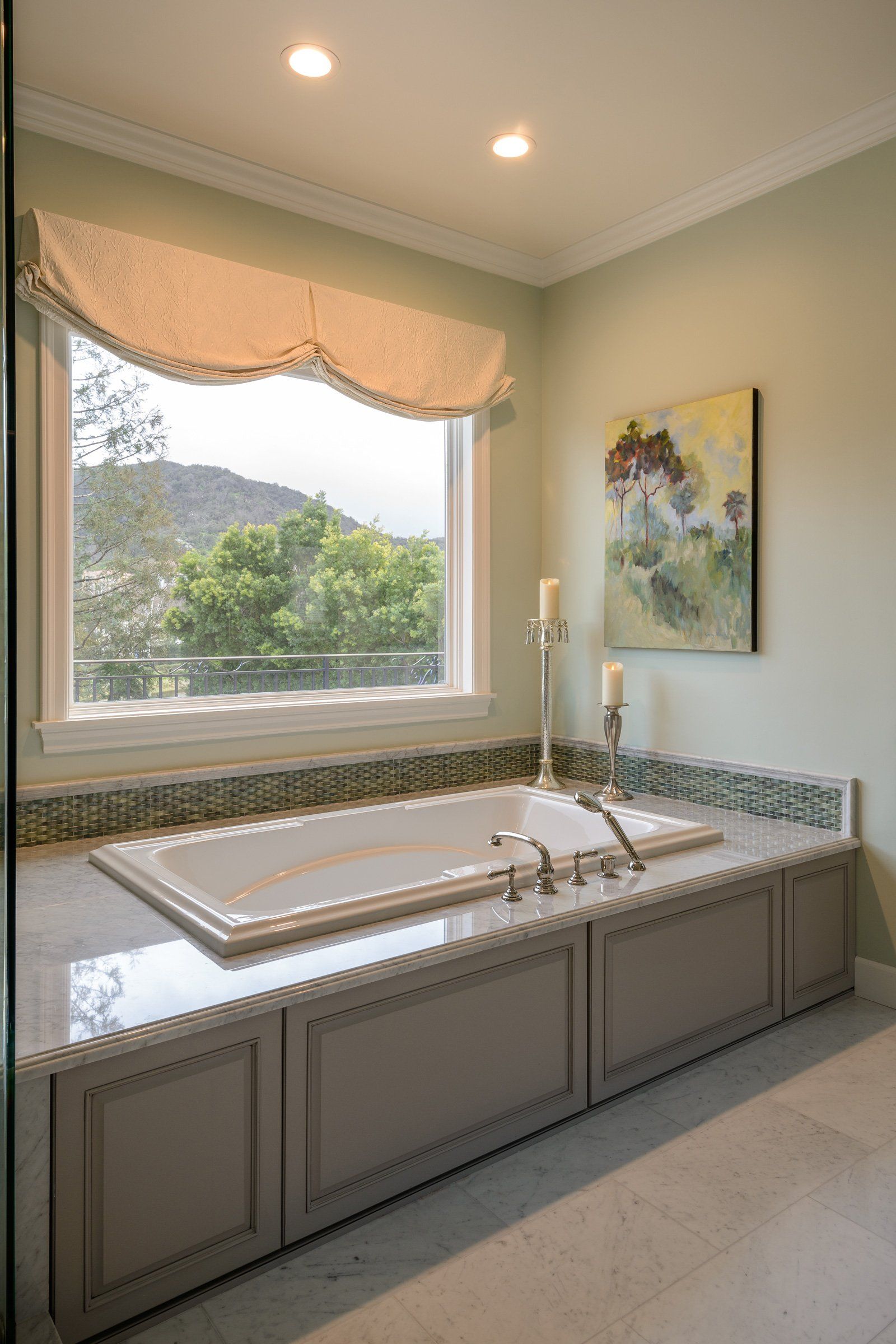 Bright bathroom vanity with double sinks, mosaic backsplash, and a window overlooking trees and hills