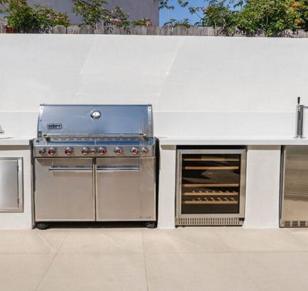 Outdoor built-in stainless steel grill and warming oven on a tiled patio against a white wall