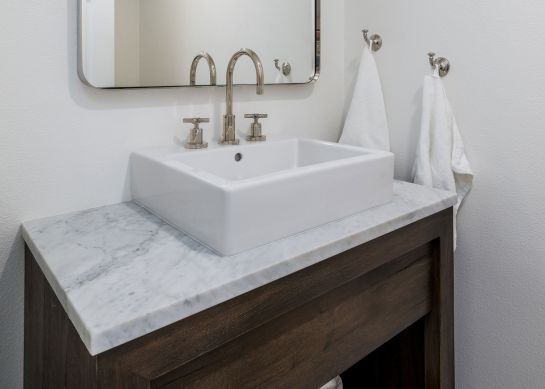 Modern bathroom vanity with marble countertop, white square sink, gold faucet, and hanging towels