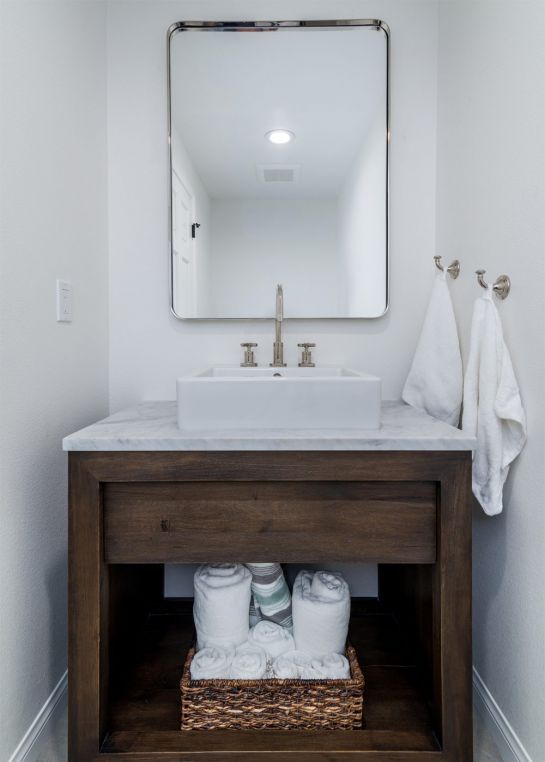 Modern bathroom vanity with marble sink, mirror, and towels on wall hooks, plus storage basket underneath