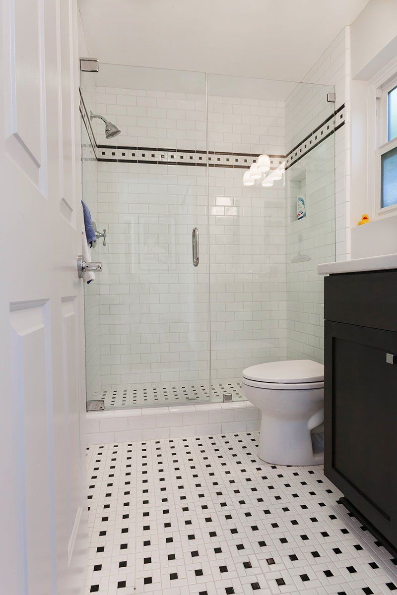 Small white bathroom with tiled shower, black-and-white floor, toilet, and dark vanity.