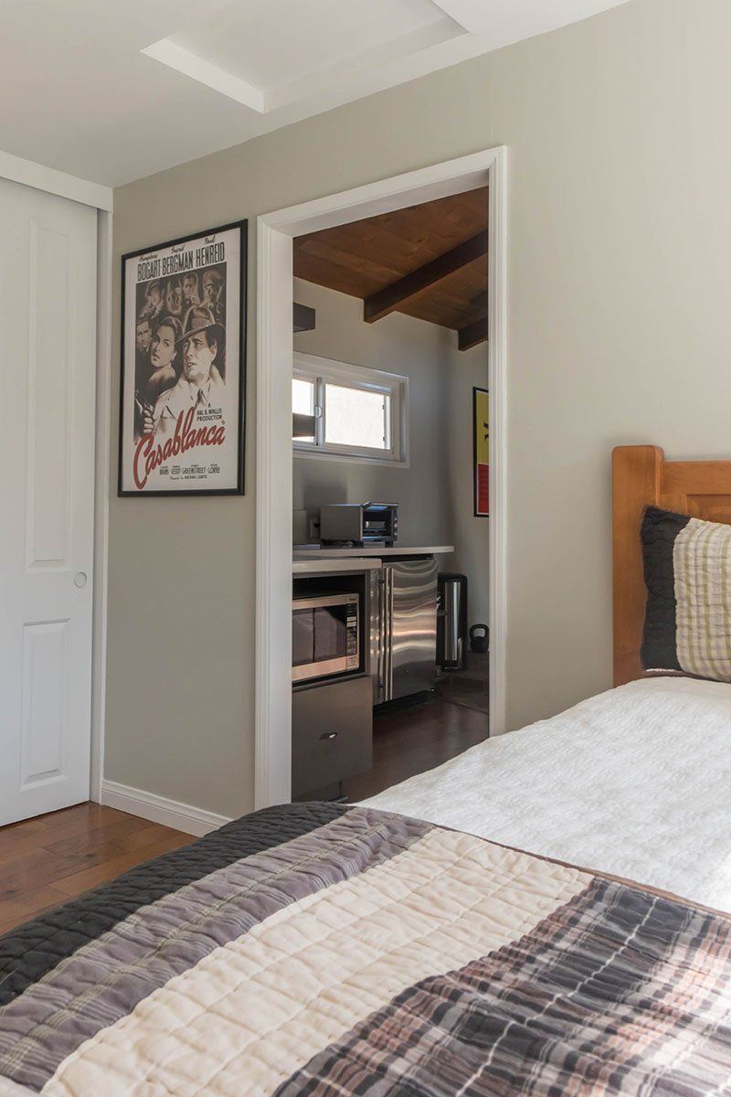 Bedroom with plaid bedspread, open doorway to a desk area, and a framed poster on the wall.