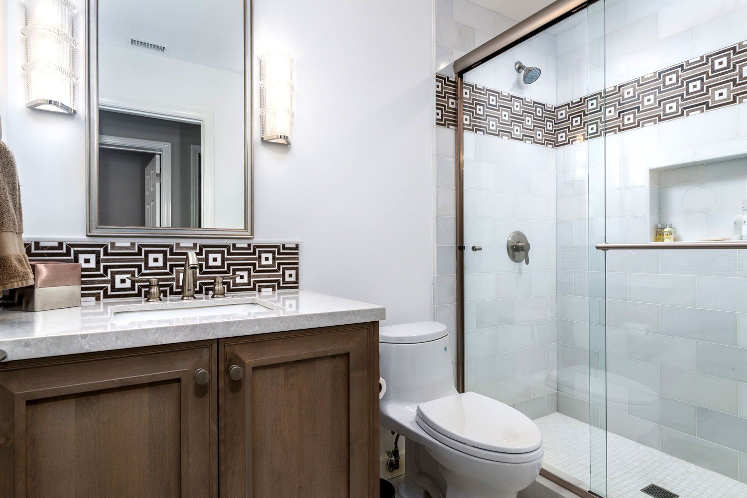 Modern bathroom with wooden vanity, large mirror, toilet, and glass-enclosed shower with decorative tile trim