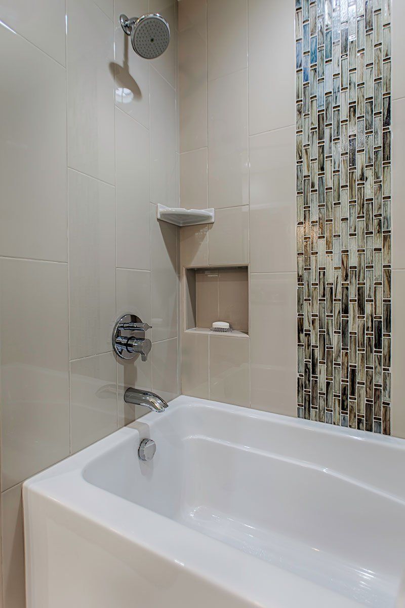 Small bathroom with white tub, shower fixtures, and a patterned accent tile wall.