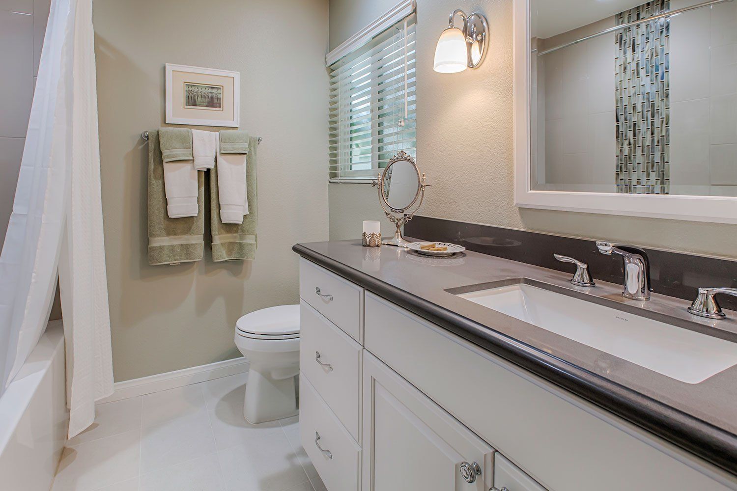 Modern bathroom with white vanity, mirror, wall sconce, toilet, and towel rack