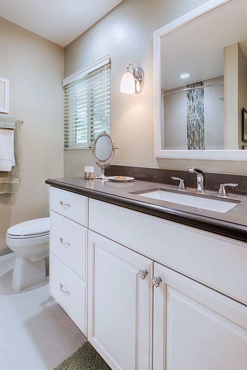 Bright bathroom with white vanity, dark countertop, mirror, window, and toilet.