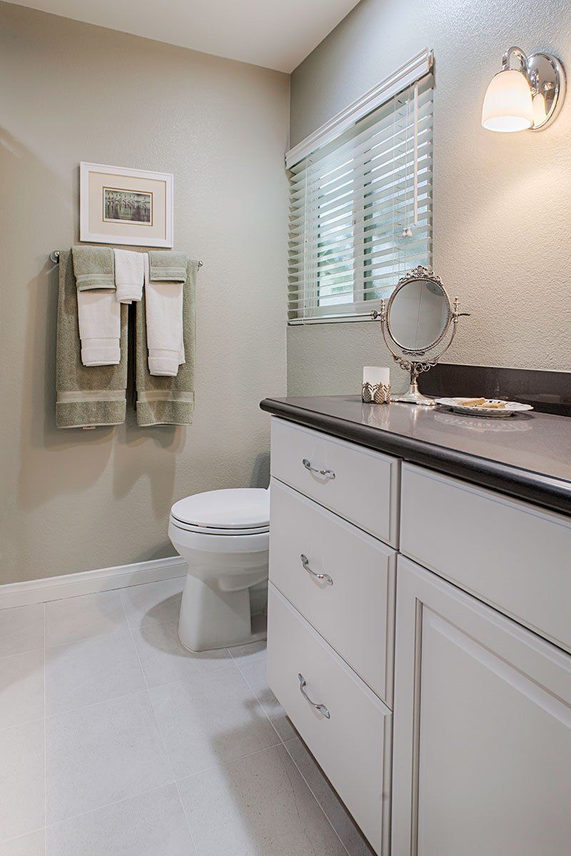 Bright bathroom with white vanity, toilet, towel rack, window blinds, and wall light.