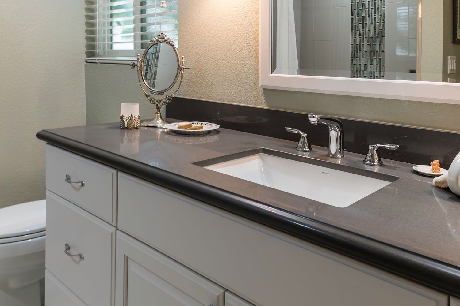 Modern bathroom vanity with black countertop, sink, mirror, and light gray cabinets
