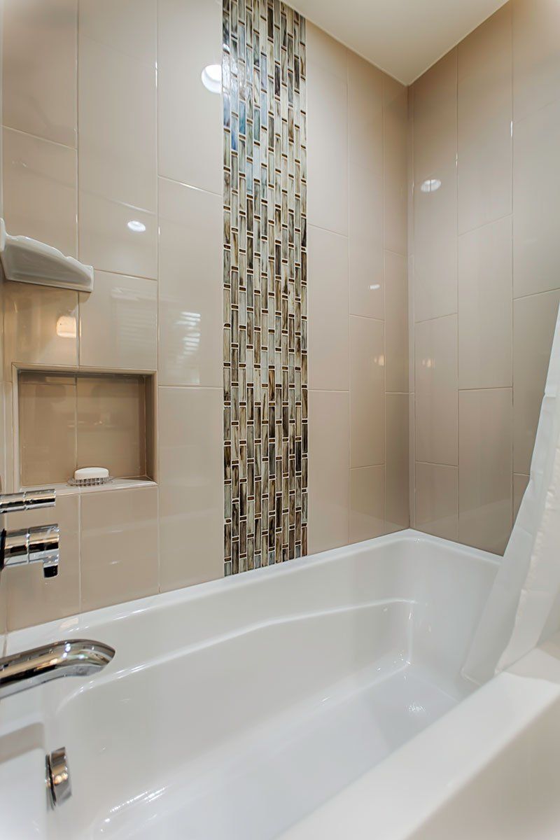 Bathroom with white tub, beige tile walls, and a narrow mosaic accent strip