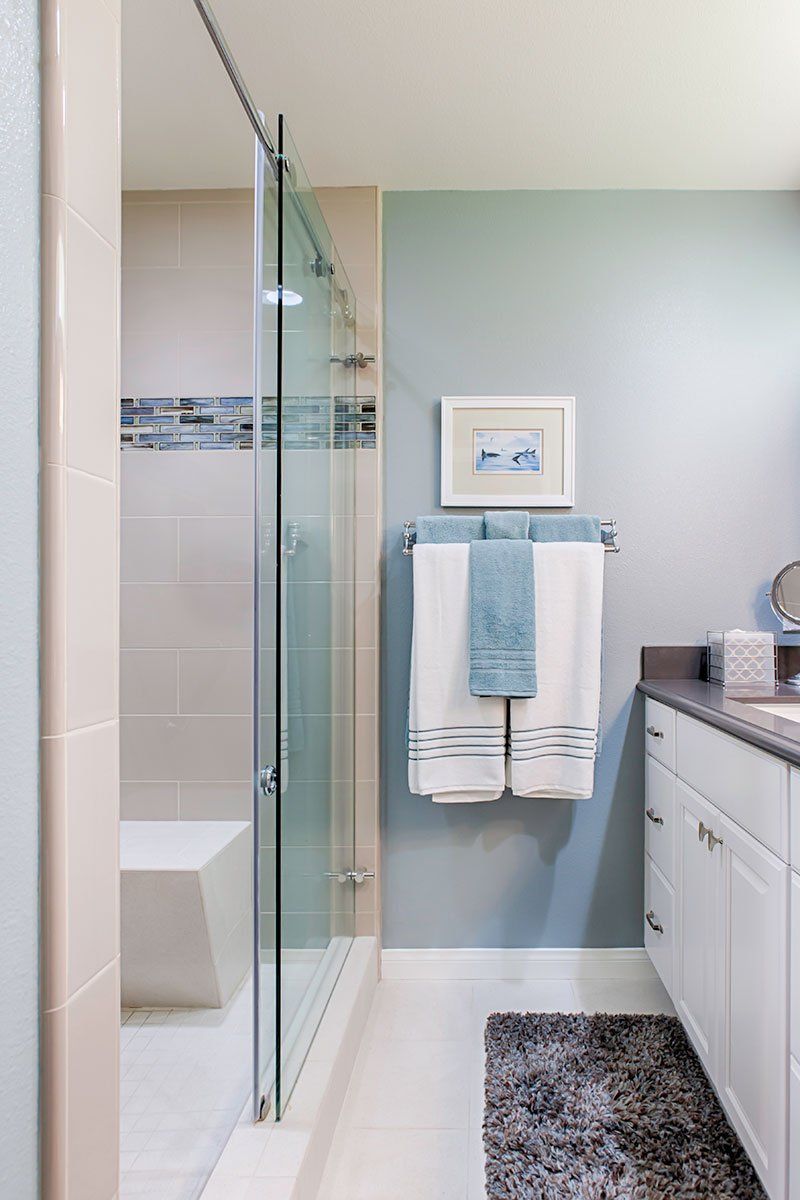 Small bathroom with glass shower, white vanity, blue walls, towel rack, and gray rug