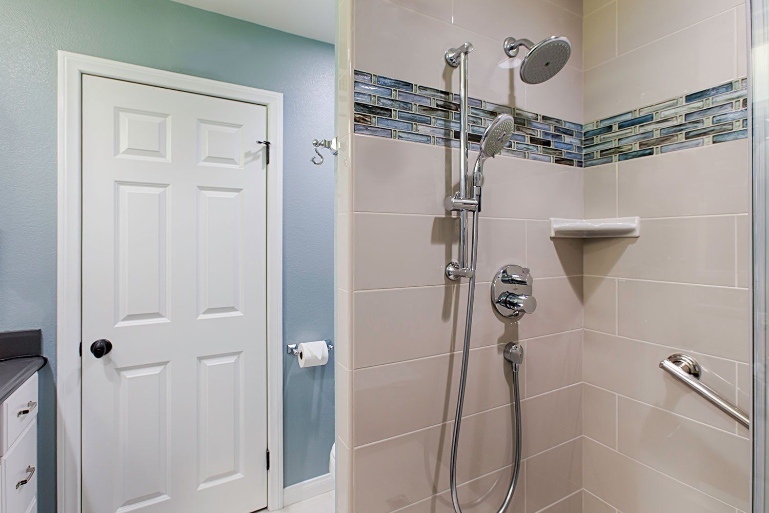 Accessible bathroom shower with grab bars, tiled walls, and a white door.