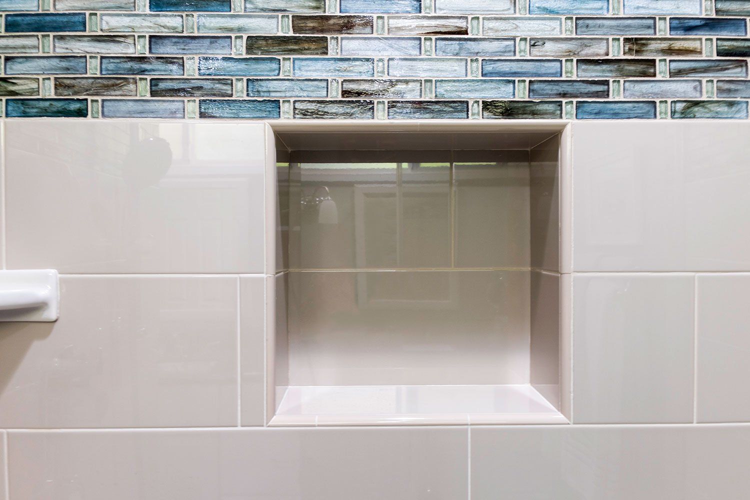 Bathroom shower niche with beige tile and blue mosaic accent border