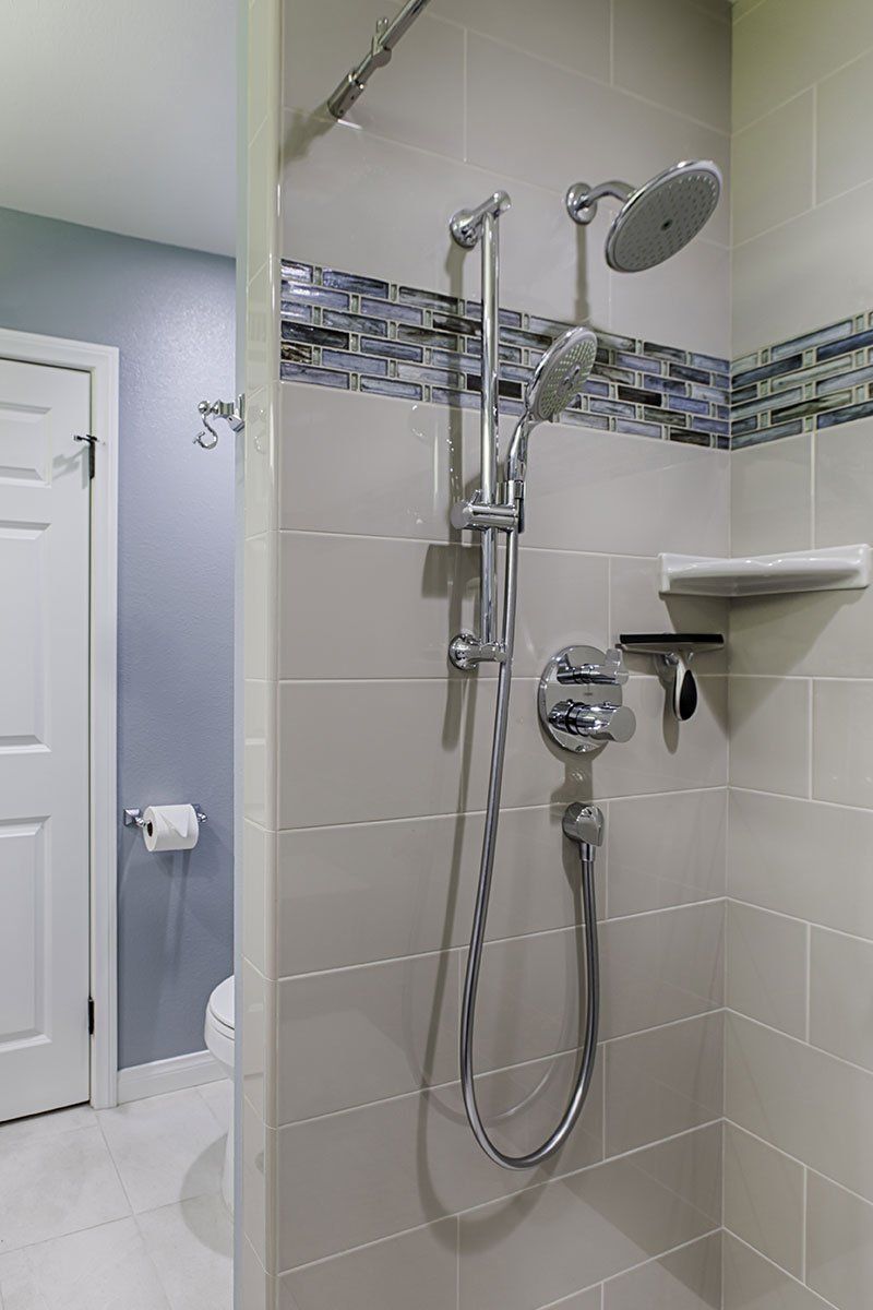 Accessible shower with chrome grab bars, handheld showerhead, and mosaic accent tile in a tiled bathroom