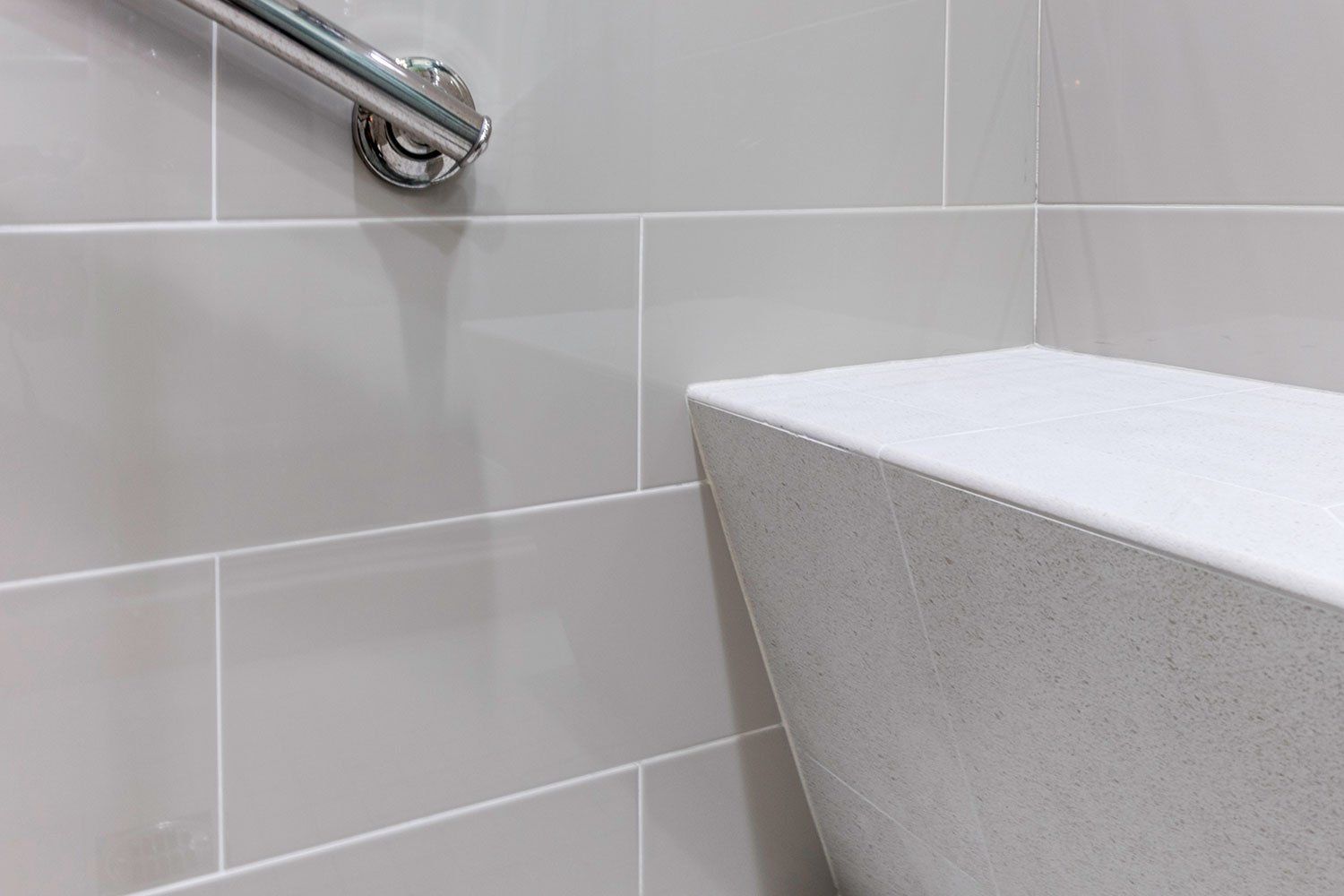 Bathroom wall with light gray tiles, a metal grab bar, and a white sink or counter edge